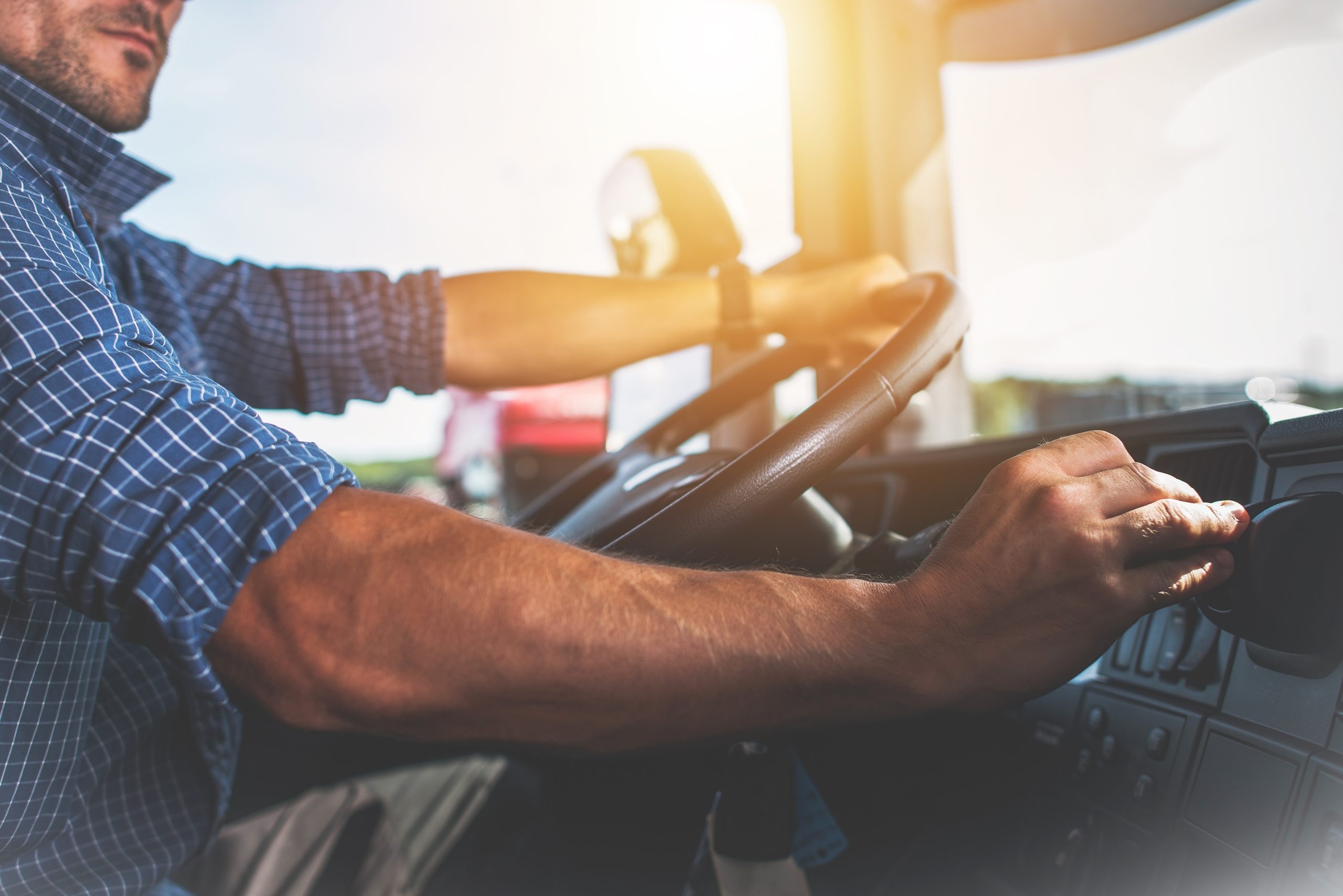 A semi-truck driver's hands on the wheel and adjusting something on the dashboard.