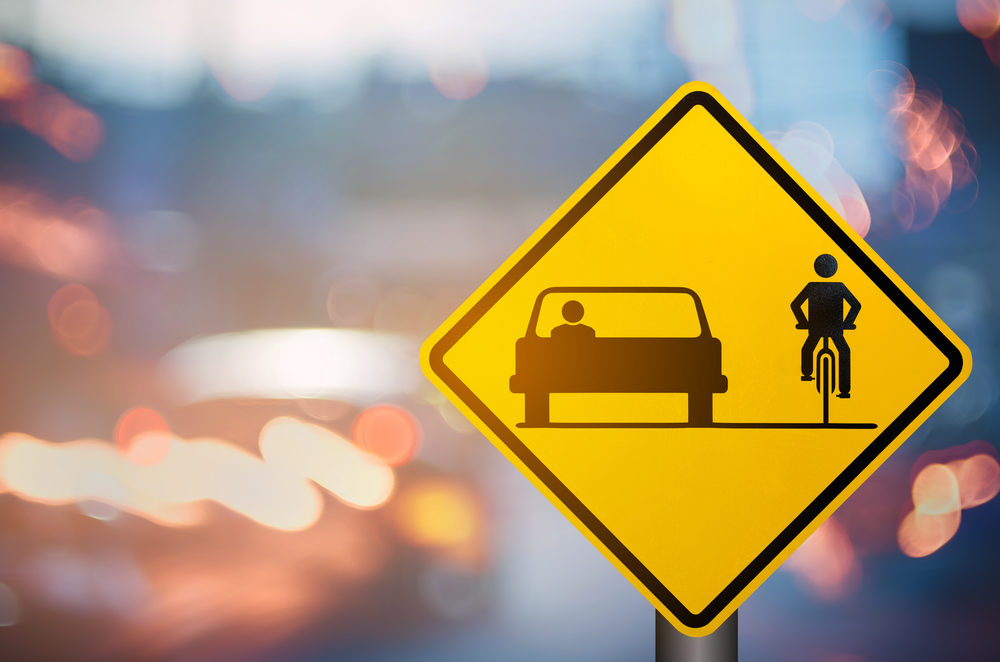 yellow warning sign for a shared roadway with a car driving alongside a bicyclist