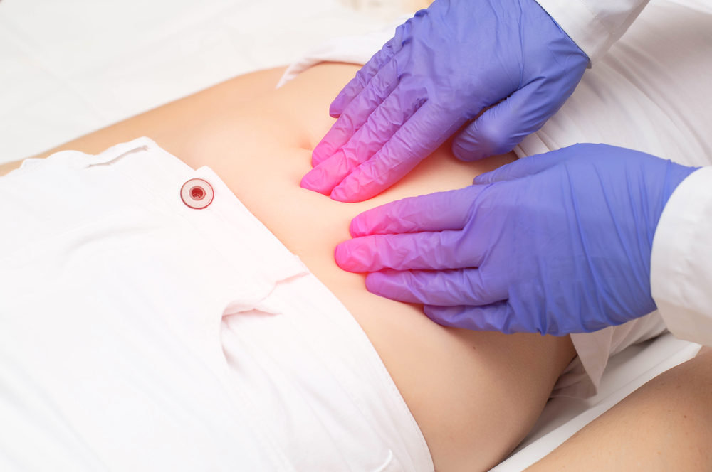 A gynecologist doctor probes the lower abdomen of a girl who has pain and inflammation of the reproductive system.
