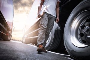 A man checking walking with a clipboard inspecting a truck's tires.