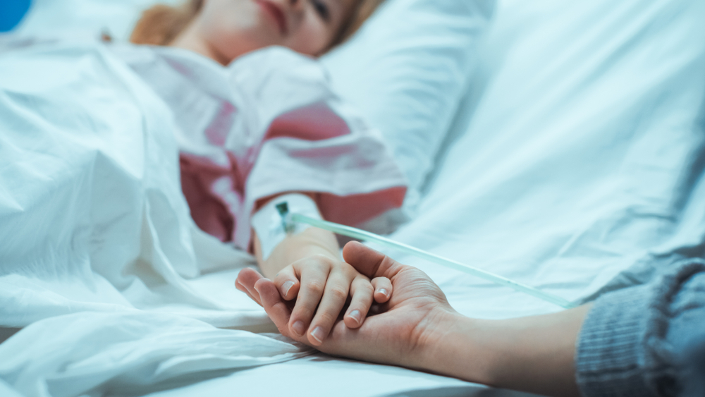 injured child in hospital bed with mother holding her hand