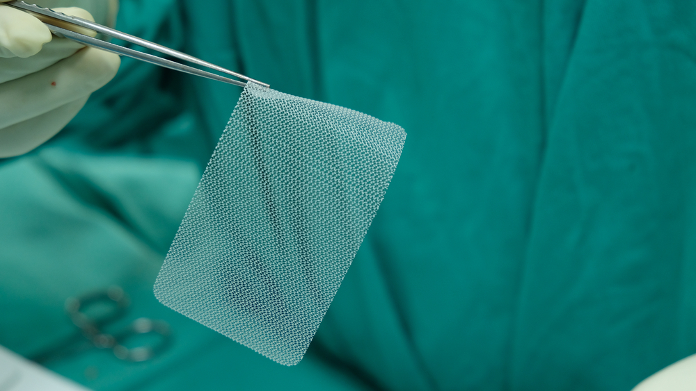 closeup of a doctor holding a hernia mesh implant with forceps