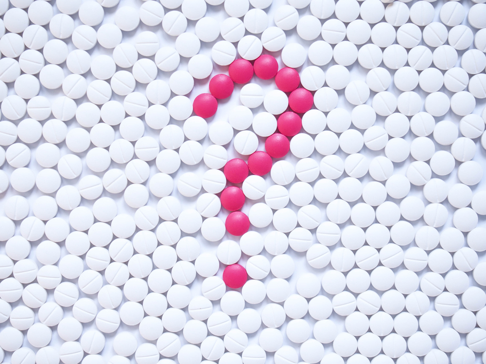 A question mark formed with pink pills surrounded by white pills