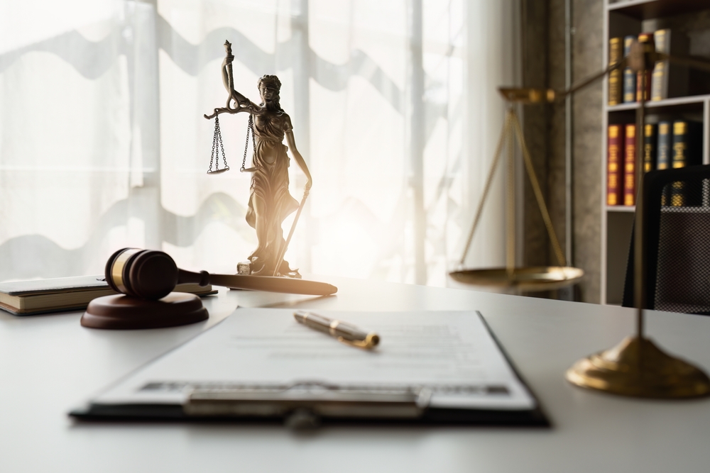 closeup view of a contract on a lawyer's desk with scales in the foreground gavel, lady justice statue and law books in background