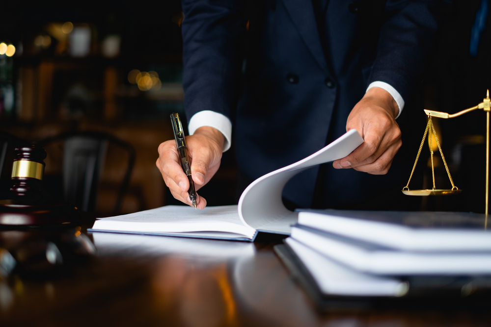 Close up of a lawyer writing in a book on his desk with a gavel and scales