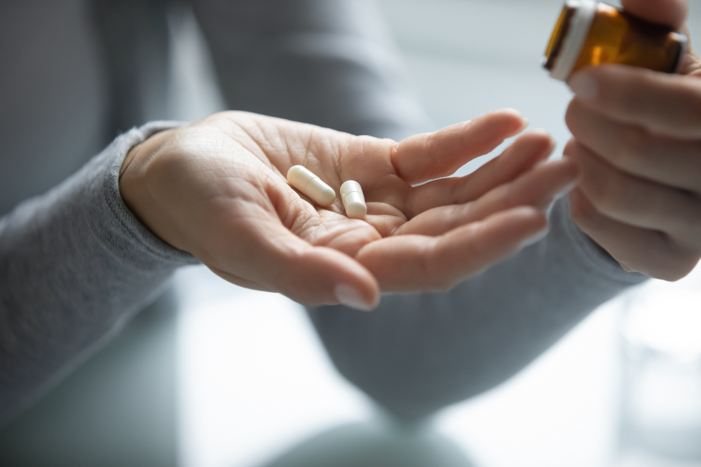 Close up of young female hands holding opened pill bottle and two soft-shelled regeneslim capsules