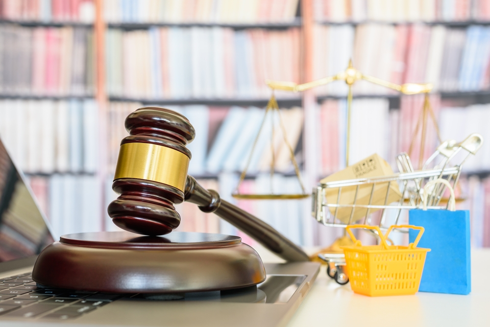 gavel on a laptop computer with shopping basket, shopping bags and a shopping cart on table with scales and book cases behind