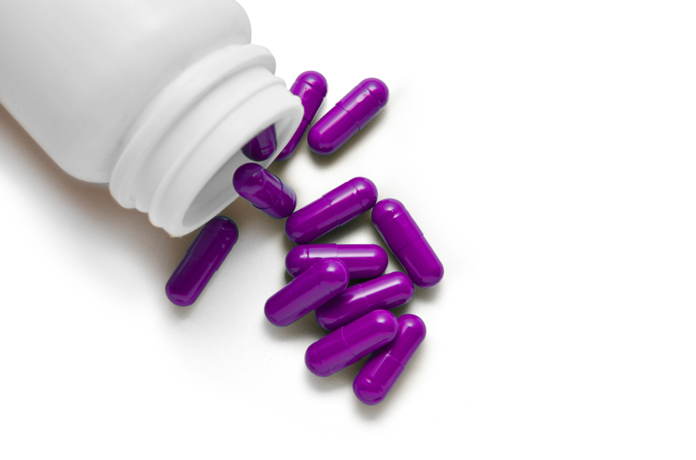 purple capsules pouring out of a white medicine bottle isolated on a white background