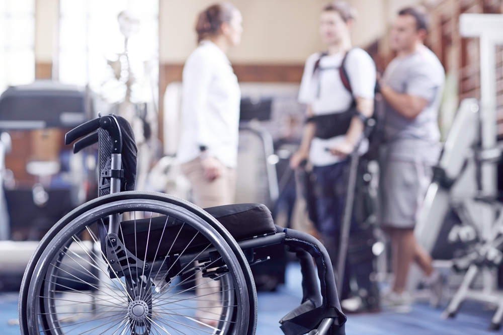 man receiving physical therapy for a spinal cord injury with a wheelchair in the foreground