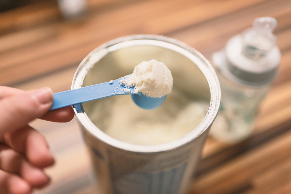 Powder baby formula and blue spoon on light background close-up.