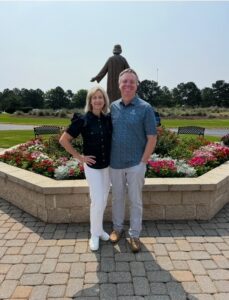 Michelle and Richard Schlueter standing outside in front of a statue and flowers.