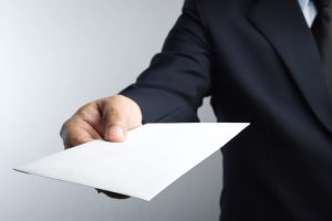 A lawyer in a dark suit holding a plain white envelope in his hand.