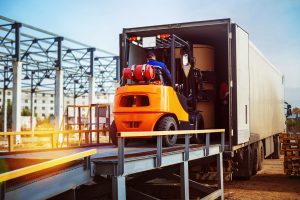 Forklift is putting cargo from warehouse to the back of a truck outdoors