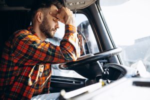 A tired truck drier resting his head in his hands behind the wheel.