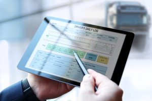 A safety manager's hands holding a tablet showing truck driver electronic logbooks on a tablet.