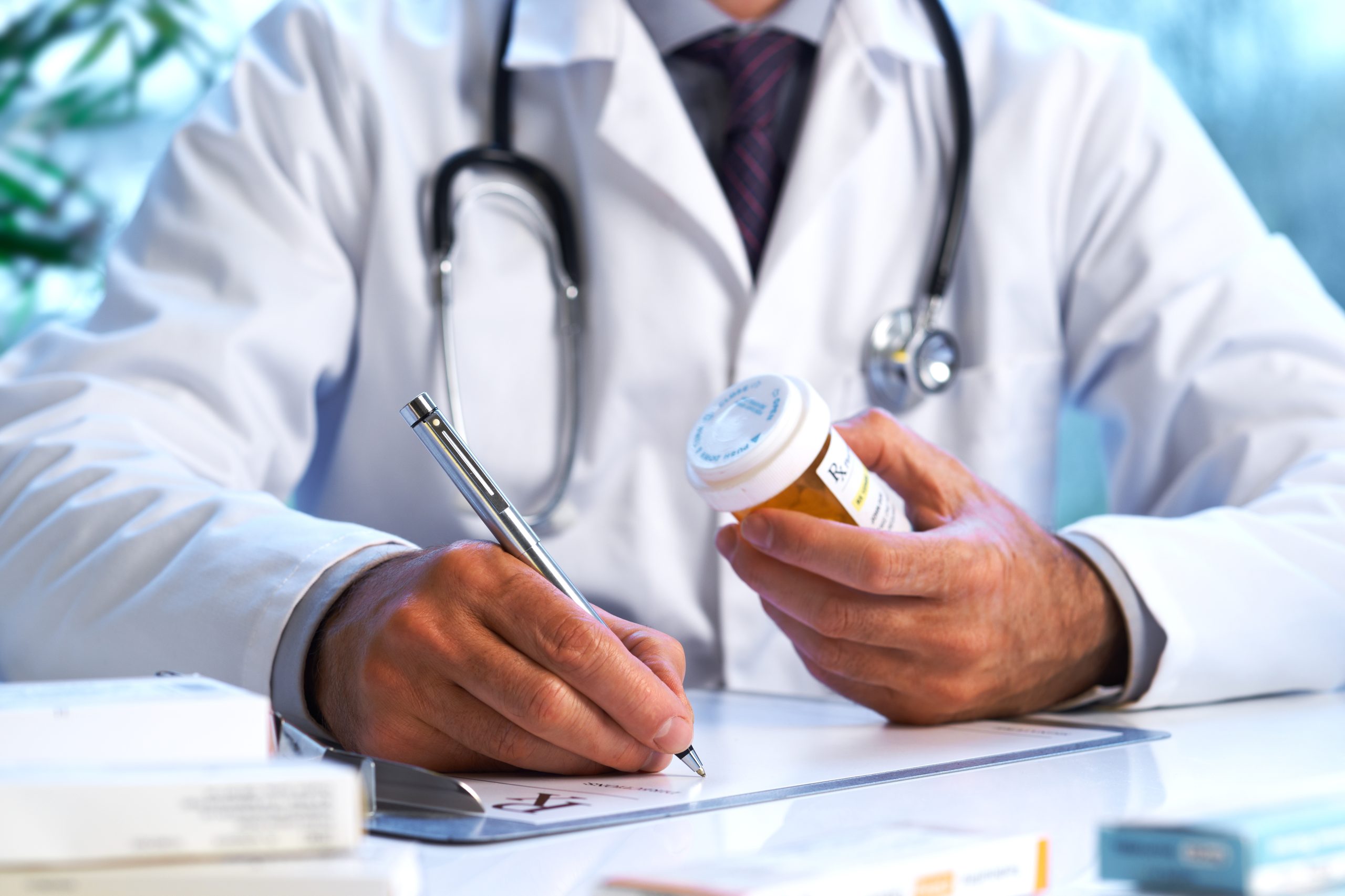 Doctor writing a prescription and holding a pill bottle in his hand.